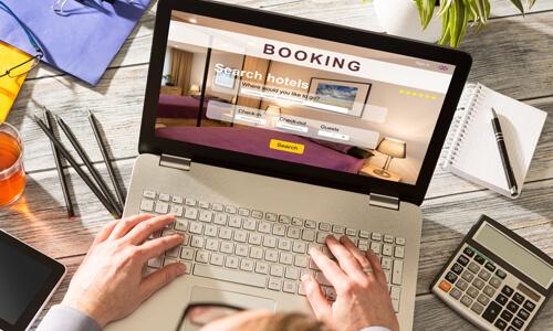 Laptop with hotel bookings on screen - hands on keyboard looking for a good hotel deal.