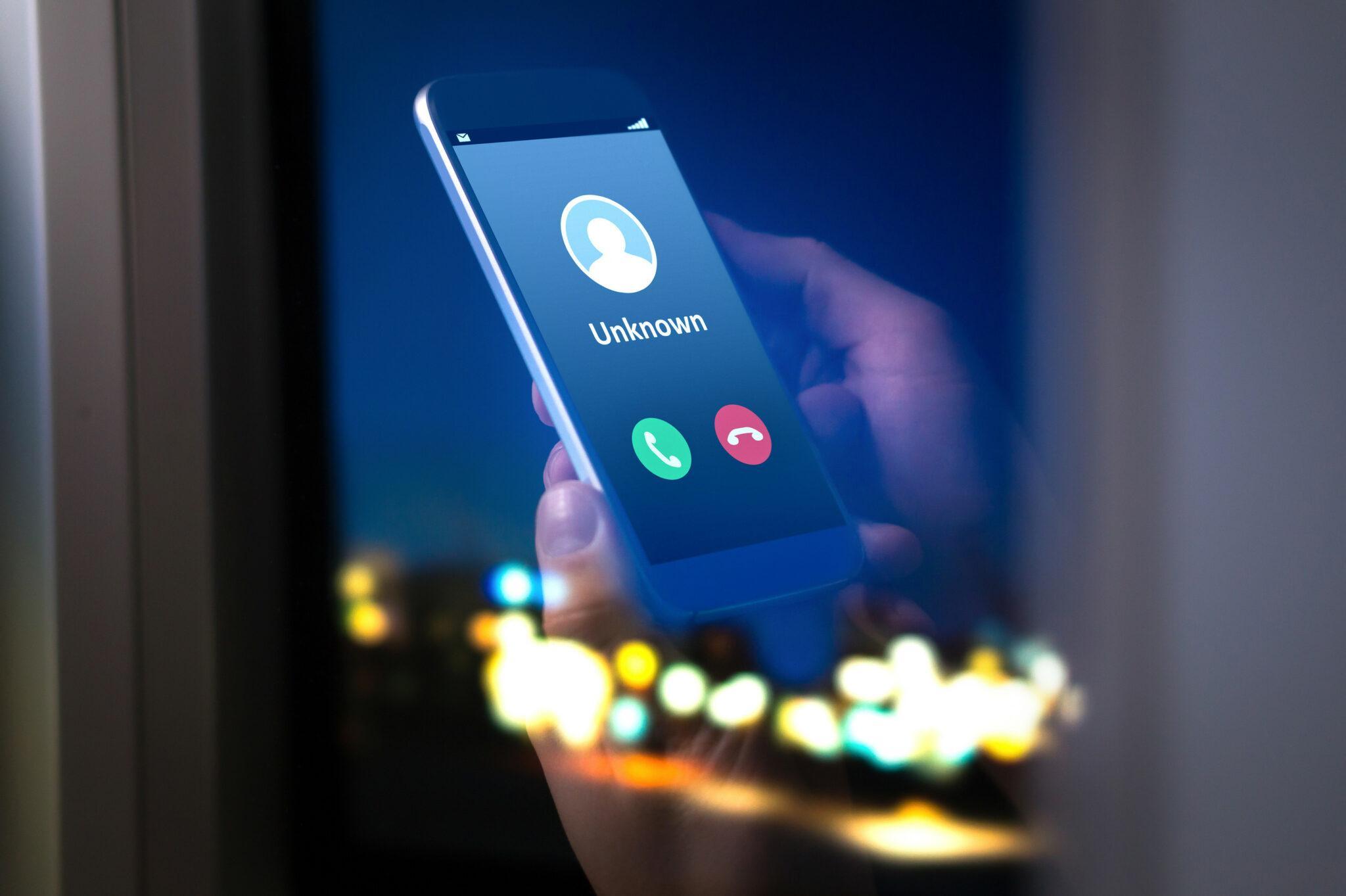 A smartphone screen displaying an incoming call from 'Unknown,' with options to accept or decline the call. The image is set against a dark background with blurred city lights, creating a mysterious and tech-focused atmosphere.