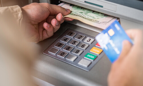 Close up of man's hand holding dollar bills from ATM machine and ATM card in the other hand.