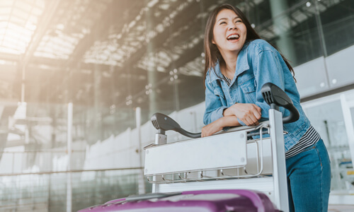 Young woman smiling in airport terminal with her luggage.
