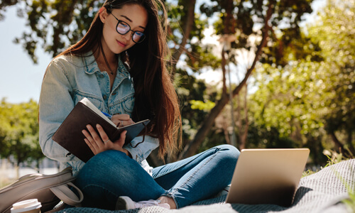 College student sitting outdoors with her laptop and schoolbooks.