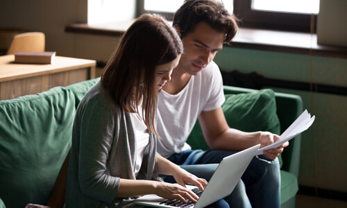 Couple seated on couch reviewing their finances.