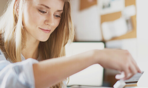Woman sitting at desk and smiling at her debit card.