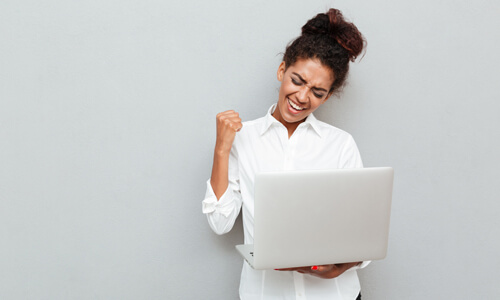 Woman holding laptop in hand and cheering because her direct deposit came through.