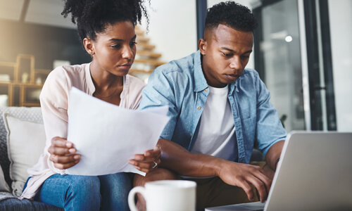 Couple seated on couch with laptop reviewing their credit report, disputing an error.