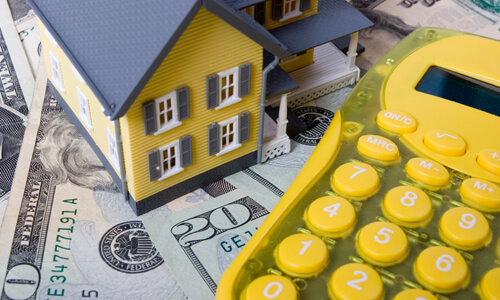 Yellow model house and yellow calculator on dollars bills.