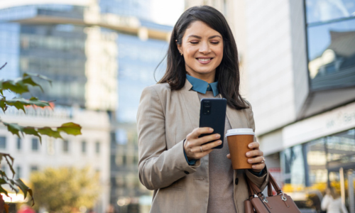 Woman outside, looking at her phone to check the savings she earned from HighMarq Savings.
