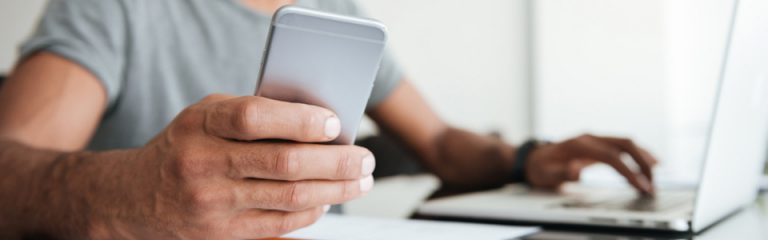 Man on laptop and mobile device, smiling because his check just cleared.