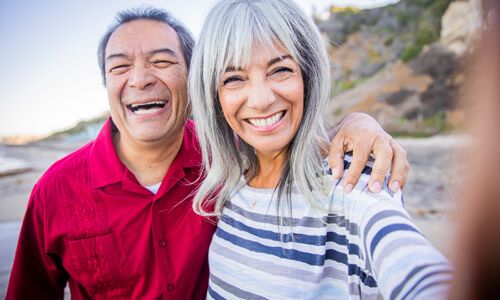 Retired couple smiling at the camera standing on beach.