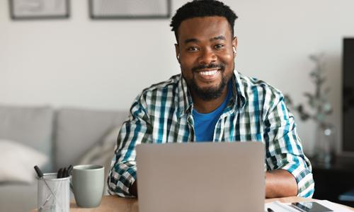 Young smiling man, working from home on his laptop, embracing New Work mentality.