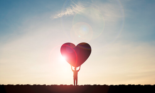 Silhouette of man at sunset holding a giant heart, illustrating philanthropy.