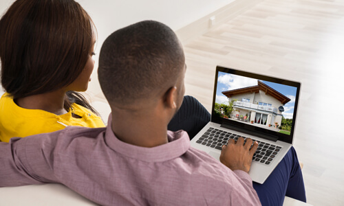 Couple seated on couch looking at new homes on their laptop.