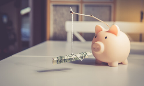 Piggy bank with dollar on a fishing pole in front of it, illustrating savings motivation.