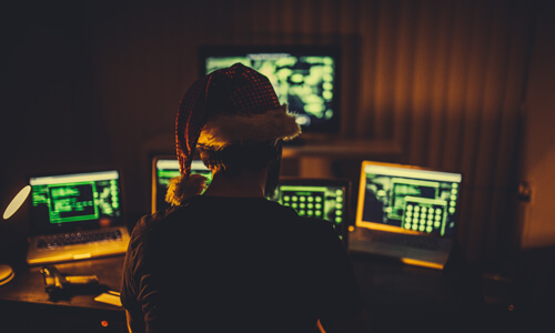 Scammer wearing santa hat looking at computer screens.