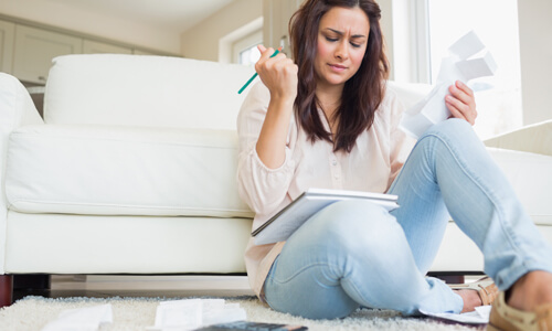 Stressed woman sitting on living room floor, looking at all of her bills.