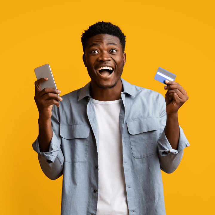 A young man on a yellow background, excitedly holds his Quorum Mastercard and cell phone.