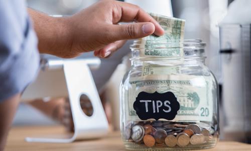 Tip jar with hand dropping a twenty dollar bill into the jar.