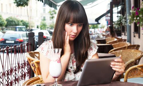 Young woman on vacation looks at tablet in concern, worried she may be victim of scam.