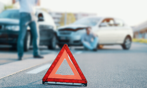 Two people in a car accident, one on the phone calling the police.