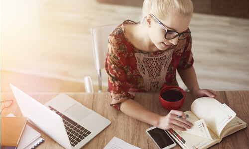 Closeup of woman using calendar, along with her phone and laptop.
