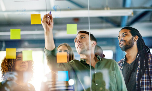 Graduate students at internship, looking at post-it notes on window.