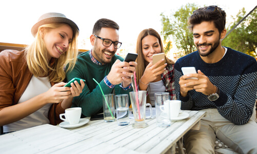 Group of friends seated around restaurant table, splitting check with their mobile devices.