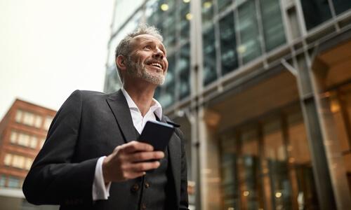 Businessman in 50s walking down street with mobile phone, ready for interview.