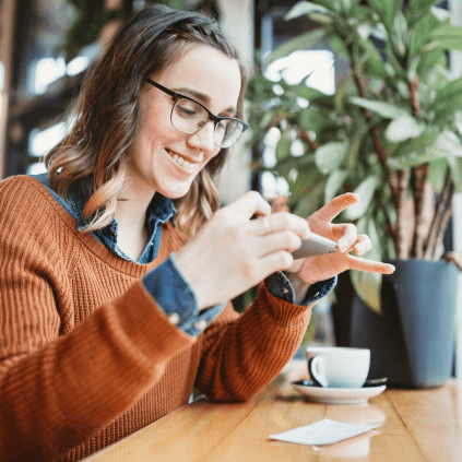 Woman is sitting at a table with a cell phone. She is taking a photo of a check for a remote deposit.