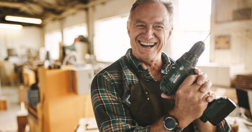 Happy semi-retired man at work in his shop, holding a drill.