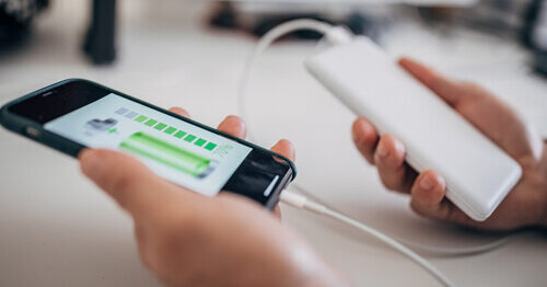 Hands charging a mobile device with a portable power device, a way to stay cybersafe when traveling.