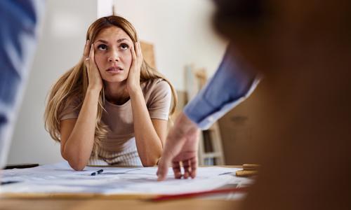 Worried woman talking about blueprint problems with a contractor (and possible scammer) in her house.