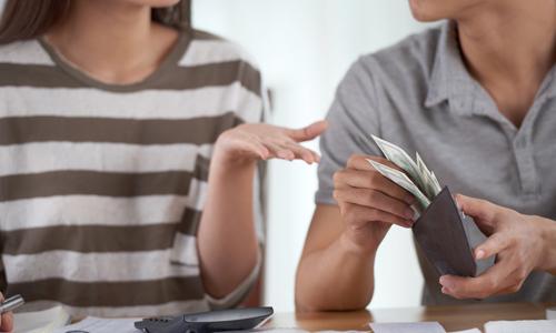 Couple discussing sharing expenses at table, with wallet, calculator and bills.