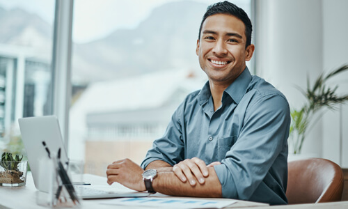 Young, well-dressed man at office desk, smiling at office.