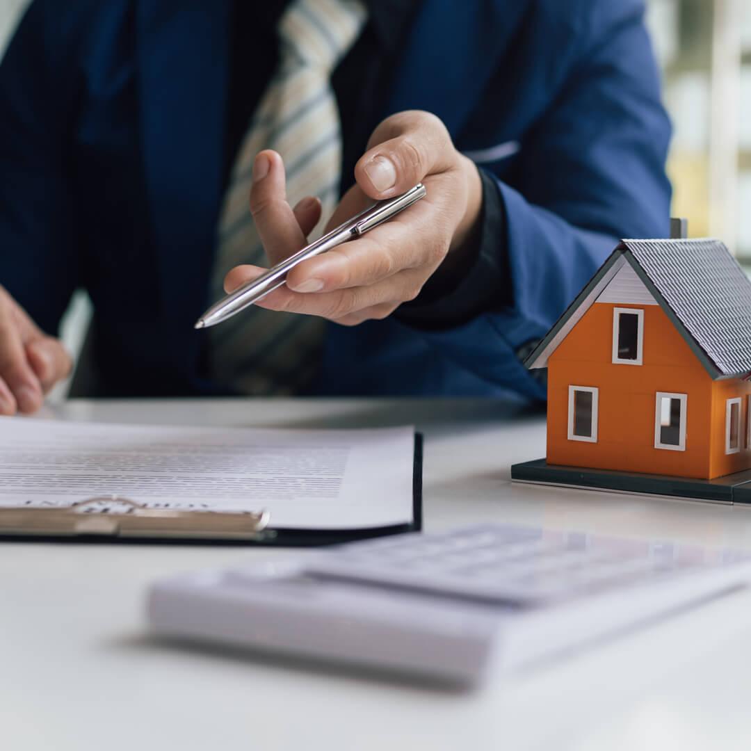 Loan Subordination Agreement on table, next to a model home, and a man motioning camera to sign agreement.