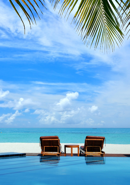 Two lounge chairs on the edge of a hotel pool with the ocean in the background.