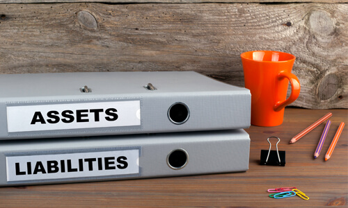 Two binders, one labeled "Assets" and the other labeled "Liabilities" lying on a desk.