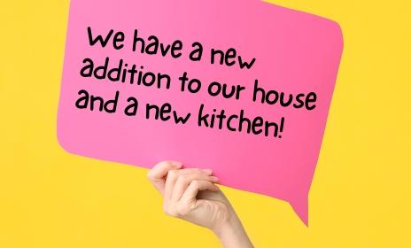 A hand holding a sign that says "We have a new addition to our house and a new kitchen."