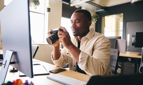 Man sits at his computer monitor, examining his new digital camera, his latest hobby.