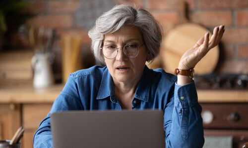 Older woman at her laptop looking concerned after possibly falling victim to a survey scam.