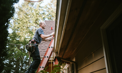 Man on ladder making repairs to his home roof.