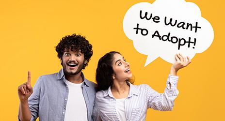 Couple holding a sign saying "We Want to Adopt" and considering a HELOC for their funding needs.